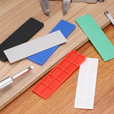 Assorted color plastic shims for leveling, including red, green, and black shims, for home improvement projects.