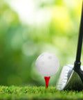 Golf club next to a white 50PC Plastic Golf Training Ball 42 mm on red tee, on green grass background.