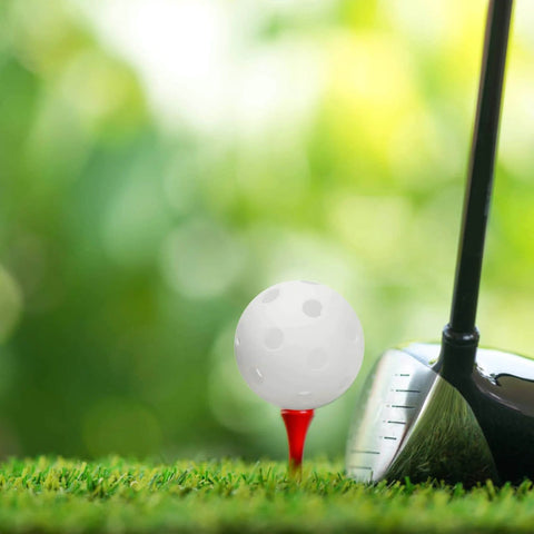Golf club next to a white 50PC Plastic Golf Training Ball 42 mm on red tee, on green grass background.
