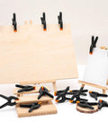 24 Pack 3.5 Inch Plastic Spring Clamps Black Heavy Duty Clips, shown holding wood and canvas, used for crafts and photography.
