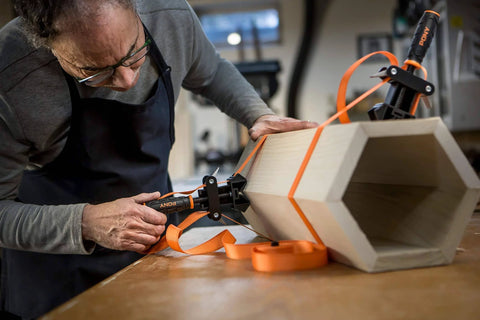 Man using Adjustable Clamp Pony 1225 Rapid Acting Band Clamp with Non Marring 1x1 Inch Jaws on hexagonal wood shape
