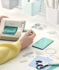 Person using Portable Die Cutting And Embossing Starter Kit For Arts And Crafts Scrapbooking And Cardmaking On The Go Sizzix Sidekick 661770 Included Compact Manual Cutter With 6.35 cm And 2.5 Inch Openings White on a desk