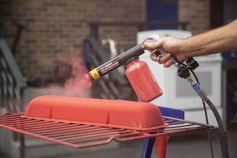 Person using HotCoat PCS-250 Powder Coating System with red powder on a metal part, highlighting dual voltage gun action.