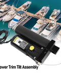 Power trim tilt assembly for outboard motor; black cylindrical unit with yellow cap and wiring, marina boats visible.