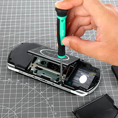 Using the 104 Piece Home Repair Tool Set With Easy Carrying Pouch For DIY Projects And Everyday Fixes Includes Hammer Pliers Magnetic Screwdrivers And Bits Wrenches Utility Knife Level And More In A Turquoise Portable Kit, a hand uses a screwdriver to open a portable gaming device on a cutting mat.