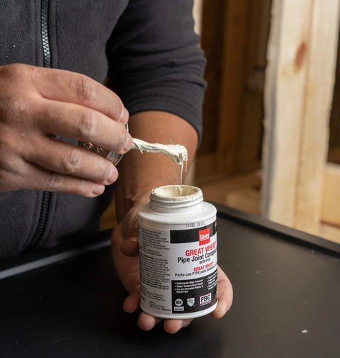 Person holding Pro Grade Pipe Joint Compound with PTFE brush, 8 oz, white non-hardening paste for threaded joints, Oatey 31231
