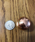 Unique Metals Pure Copper Sphere 1-1/8" next to a quarter for size comparison, on a wood surface; used for healing and decorative purposes.