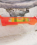 Close-up of a red acrylic line level tool placed on a stone surface, part of the Five Piece Red Hanging Line Level Set For Quick Layout.