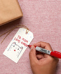 Hand using fine point permanent marker to write on a gift tag, showing bold, precise lines with quick-drying, odorless ink.