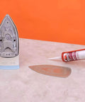 Red RTV Silicone Gasket Maker Sealant tube next to detached iron soleplate on a table, emphasizing heavy-duty automotive use