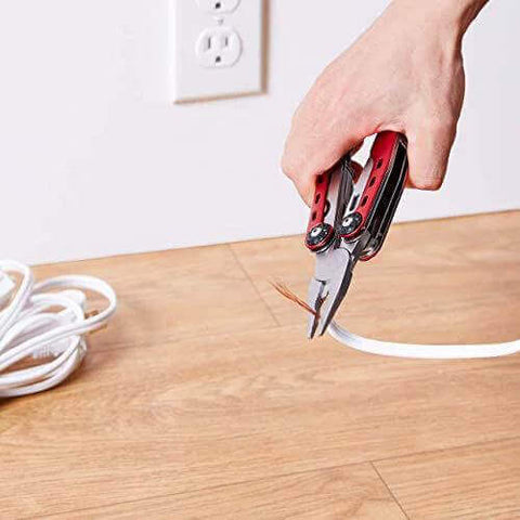 Using 10-In-1 Stainless Steel Multitool With Safety Lock And Red Nylon Sheath to cut wire on wooden floor