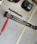Red Universal Level Holder 4 Pack with Locking Level Mounts holding a level on a StealthMounts compatible wall in a garage.