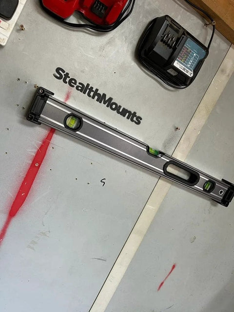 Red Universal Level Holder 4 Pack with Locking Level Mounts holding a level on a StealthMounts compatible wall in a garage.