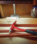 20 oz steel general purpose hammer with an ergonomic vibration-reducing grip, smooth face on a workbench next to nails and wood planks