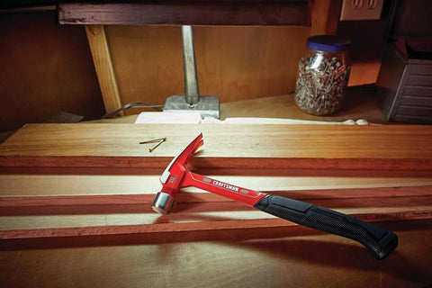 20 oz steel general purpose hammer with an ergonomic vibration-reducing grip, smooth face on a workbench next to nails and wood planks