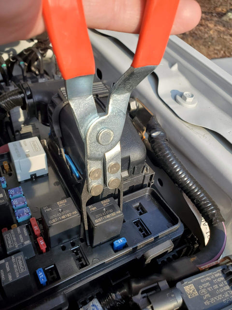 Automotive Relay Tester With Puller For 12V Cars And Trucks in use, showing relay removal with pliers inside a car's fuse box.