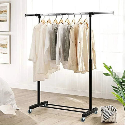 Clothes hanging on a black metal garment rack with swivel caster wheels on a wood floor in a bright room.