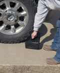 Person installing Durable Laminated Rubber Wheel Chock With Sturdy Metal Handle For Quick Safe Vehicle Blocking On Wet Slippery Or Uneven Surfaces Heavy Duty And Weather Resistant Black Vestil LWC 15 under truck tire