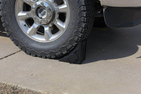 Durable Laminated Rubber Wheel Chock With Sturdy Metal Handle for Quick Safe Vehicle Blocking on a truck wheel on concrete surface.