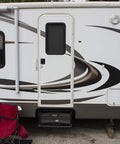 Exterior view of a recreational vehicle with a white door and abstract swirl design. A red chair sits nearby on gravel.