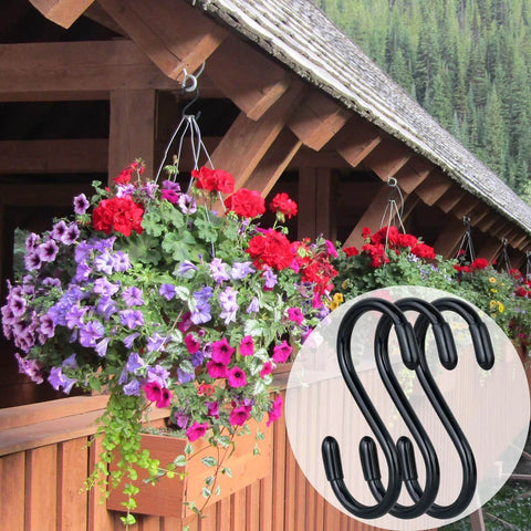 Colorful hanging flower baskets on a wooden porch with black metal S-hooks used for support, forest background visible.