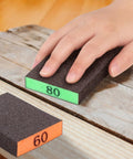 Hand using grit 80 sandpaper block on wood, with grit 60 block nearby, part of 8 Pack Sandpaper Blocks With Grits 60 80 120 220 Washable Reusable Sponges