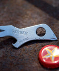 Shard 7 In 1 Keychain Multitool With Bottle Opener And Screwdriver, Lightweight Stainless Steel EDC Tool next to a bottle cap
