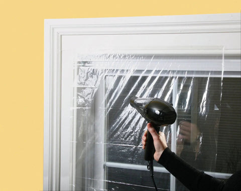 Applying Indoor Window Shrink Kit For 42 To 62 Inch Windows Clear 9 Pack Insulation Film with hairdryer on a window frame