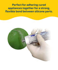 One Component Silicone Rubber Adhesive For Bonding RTV Silicone To Silicone And A Wide Range Of Substrates Including Urethane Plastics Ceramics Fabrics And More In A 3 Ounce Tube Delivers A Strong Flexible Bond That Sticks Like Crazy For Reliable Repairs being applied to a green surface by a gloved hand.