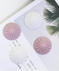 Soft silicone door stopper and wall protector cushions door impacts, reduces noise, in white and pink, placed on a book page.