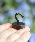 Small black magnetic hook on a person's hand in front of a blurred natural background