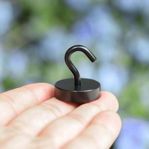 Small black magnetic hook on a person's hand in front of a blurred natural background