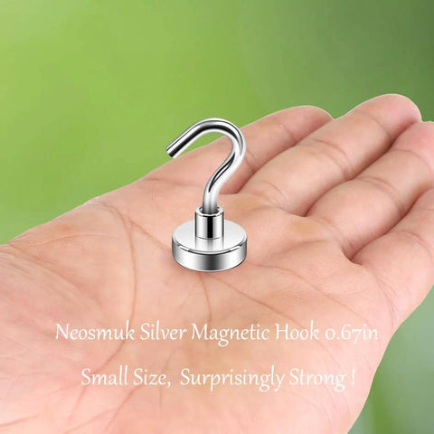 Hand holding Neosmuk silver magnetic hook, 0.67 inches, compact and strong, against a green background.