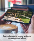 Person holding smartphone displaying footage from wire-free two-camera outdoor security kit with Sync Module 2, showing a dog outside