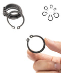 Close-up of hand holding Ultimate Snap Ring Shop Assortment Kit retaining ring, with scattered rings in background, Neiko 50458A