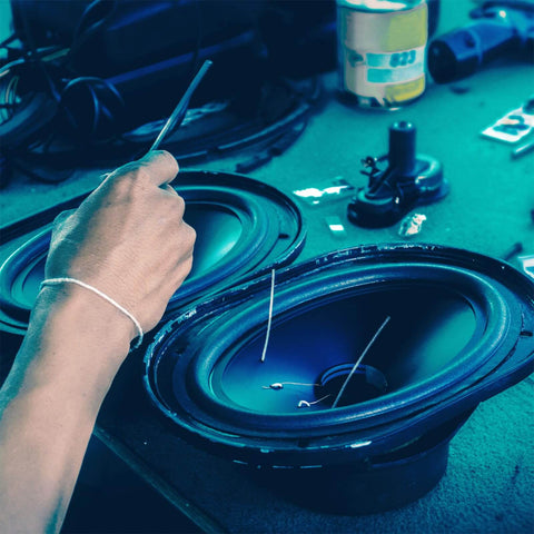 Person repairing a speaker cone on a table with tools and components nearby, focus on the speaker and repair process.