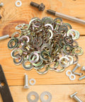 Pile of Split Lock Washer Grade Eight Thru Hardened Steel Yellow Zinc Plated 100 Pack on wooden surface with bolts and tools