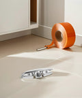 Front view of stainless steel folding boat dock cleat, 5-inch marine grade, on tiled floor beside orange tape roll