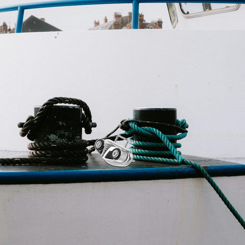 Mirror-polished stainless steel cam cleat rope lock with ball bearing on boat deck between coiled black and turquoise ropes.