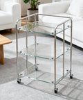 Glass shelf cart with chrome frame and wheels in modern living room setting.