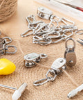 30 Pcs Single Pulley Block System 304 Stainless Steel Pulley Wheel Hanging Wire Towing Wheel with 30 Pcs Spring Snap Hook, Lifting Wire Rope Single Swivel Roller, Silver(M15) displayed on burlap surface with tools around.