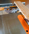 Wooden board on a table saw with stainless steel roller bracket set in the background.