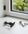 Top-down view of a black T-handle draw latch with metal mounting bracket and two screws on a white table.