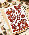 Steampunk Gear Die Cut Set For Scrapbooking And Card Making With Slick Mechanical Butterfly Embossing Stencils, Vintage Gear Frames, DIY Crafts by MAYJOYDIY displayed on a table with various decorative elements.