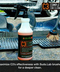 Suds Lab C3 Complete Car Cleaner 32 oz bottle with car mat and brush on concrete.