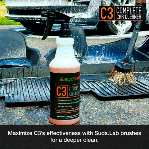 Suds Lab C3 Complete Car Cleaner 32 oz bottle with car mat and brush on concrete.