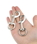 Person holding two Swivel Eye Bolt Snap Hooks For Pet Leash And Collar Heavy Duty Clips, zinc alloy construction, durable and smooth rotation.