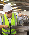 Worker in safety gear operating lathe machine in industrial workshop.