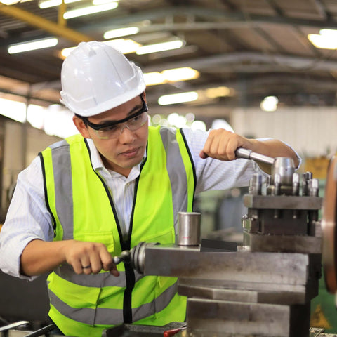 Worker in safety gear operating lathe machine in industrial workshop.