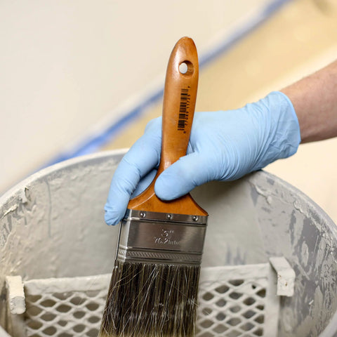 Person wearing Textured Blue Nitrile Gloves 5 Mil Powder Free Food Safe Large Box Of 100 holding a paintbrush over a paint can